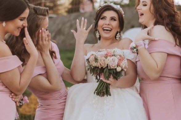 a bride shows of her ring while her bridesmaids pose with her